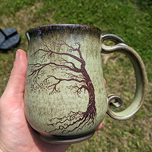A green ceramic mug with a spiraling branched tree that matches the handle